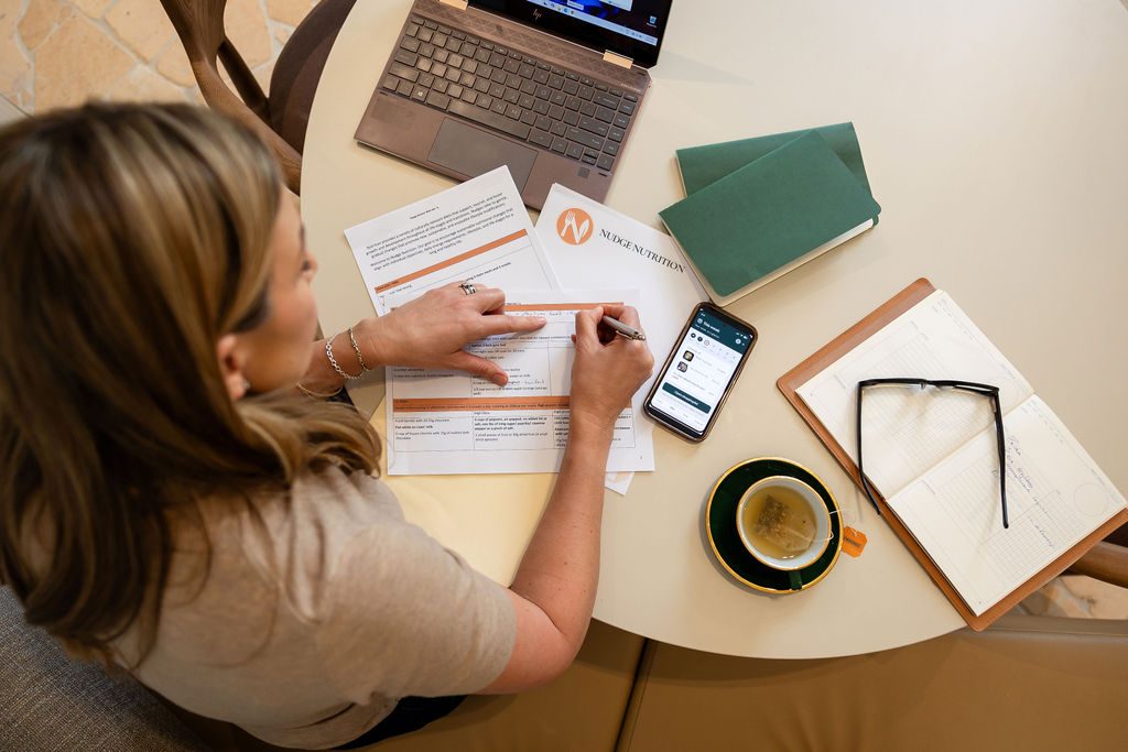 Nikki working through a client plan with her notes, laptop and the app to hand